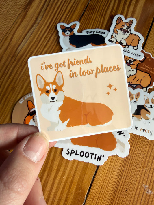 "Friends in Low Places": Close-up of a sticker showing a low-profile corgi with the punny text "I’ve got friends in low places."