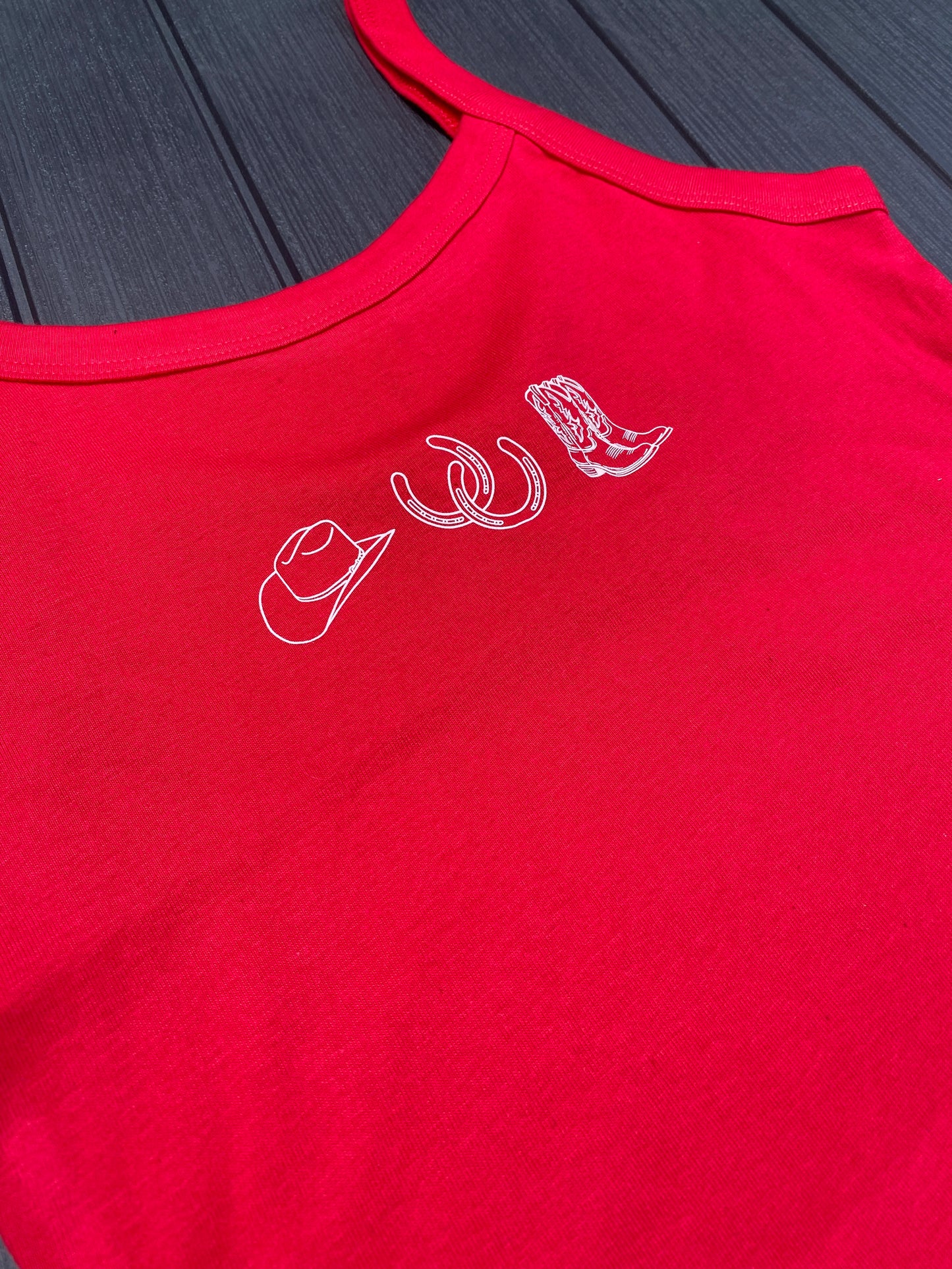 Flat lay of red tank top with white cowgirl collage graphic design on a dark surface