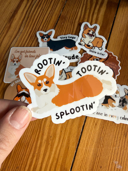 "Rootin', Tootin', Splootin'": A hand holds a sticker of a corgi in a "sploot" position (legs stretched out) with the text "Rootin', tootin', splootin'."