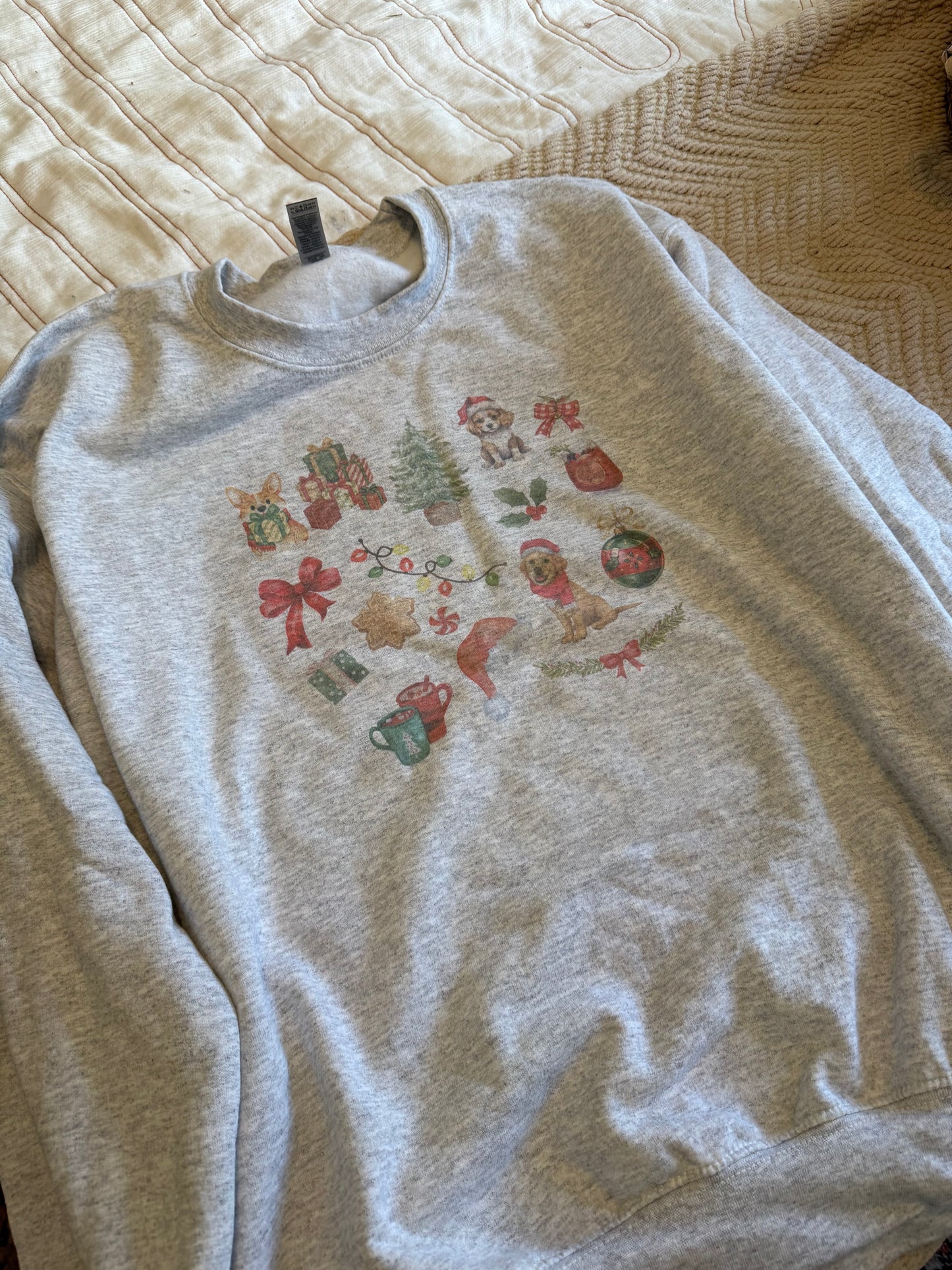 Flat lay of Gildan 18000 ash Christmas dog sweatshirt with watercolor holiday dog collage, cozy winter dog lover clothing, neutral aesthetic Christmas apparel, soft fleece crewneck for holiday gifts, displayed on white and tan bed for clean modern look.