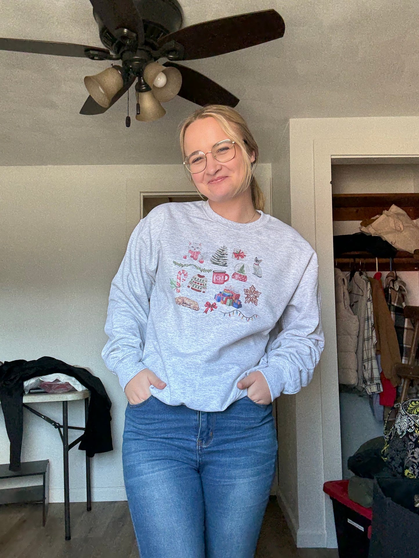 woman modeling watercolor cat christmas collage sweatshirt in ash gray, gildan 18000 crewneck with whimsical holiday cat artwork, cute christmas cat lover gift clothing, cozy winter loungewear outfit inspiration with jeans, aesthetic christmas cat sweater design