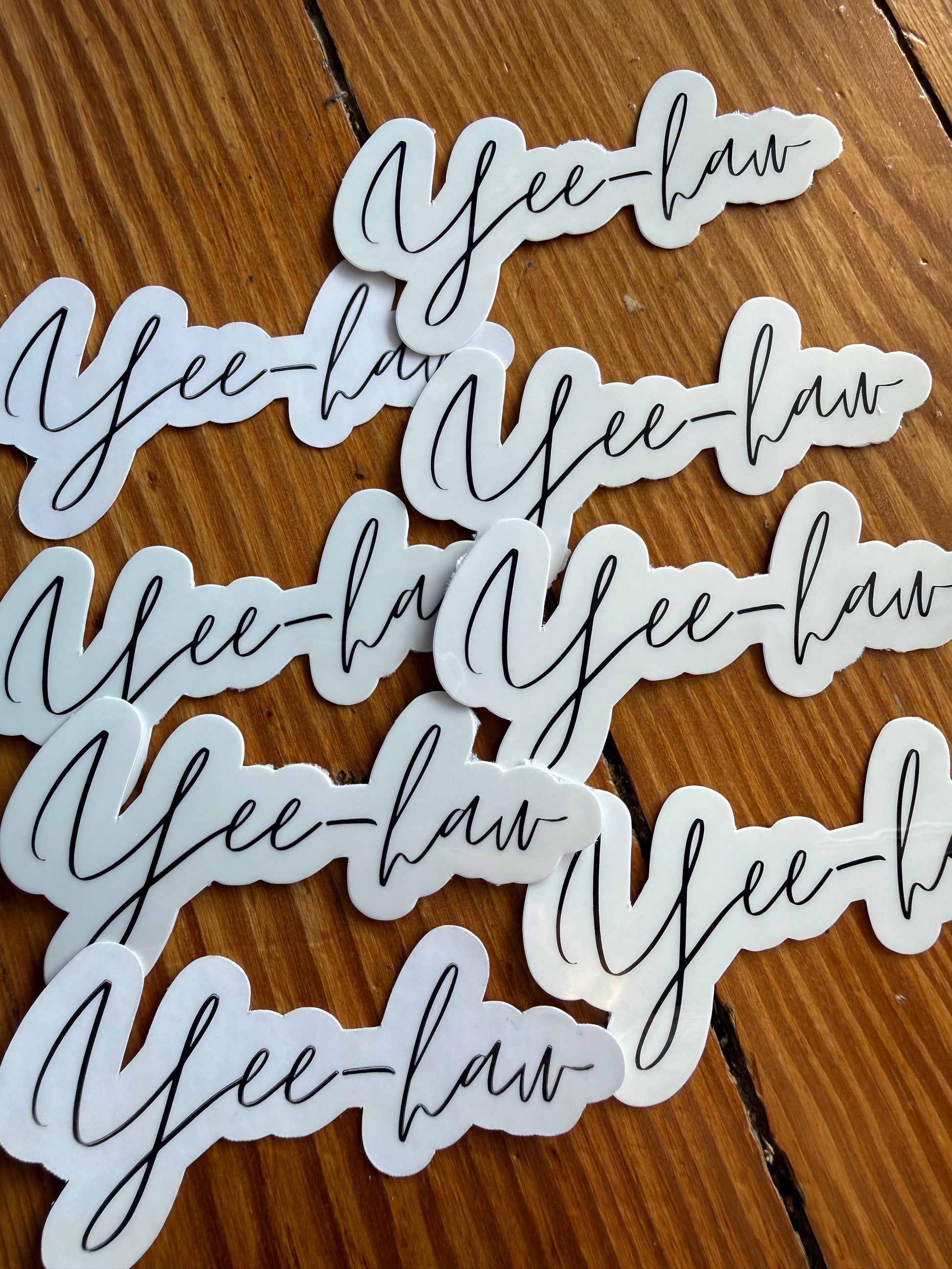 A sharp close-up of a glossy "Yee-haw" sticker held toward the camera, emphasizing the 1.5-inch height and smooth, professional die-cut edges.