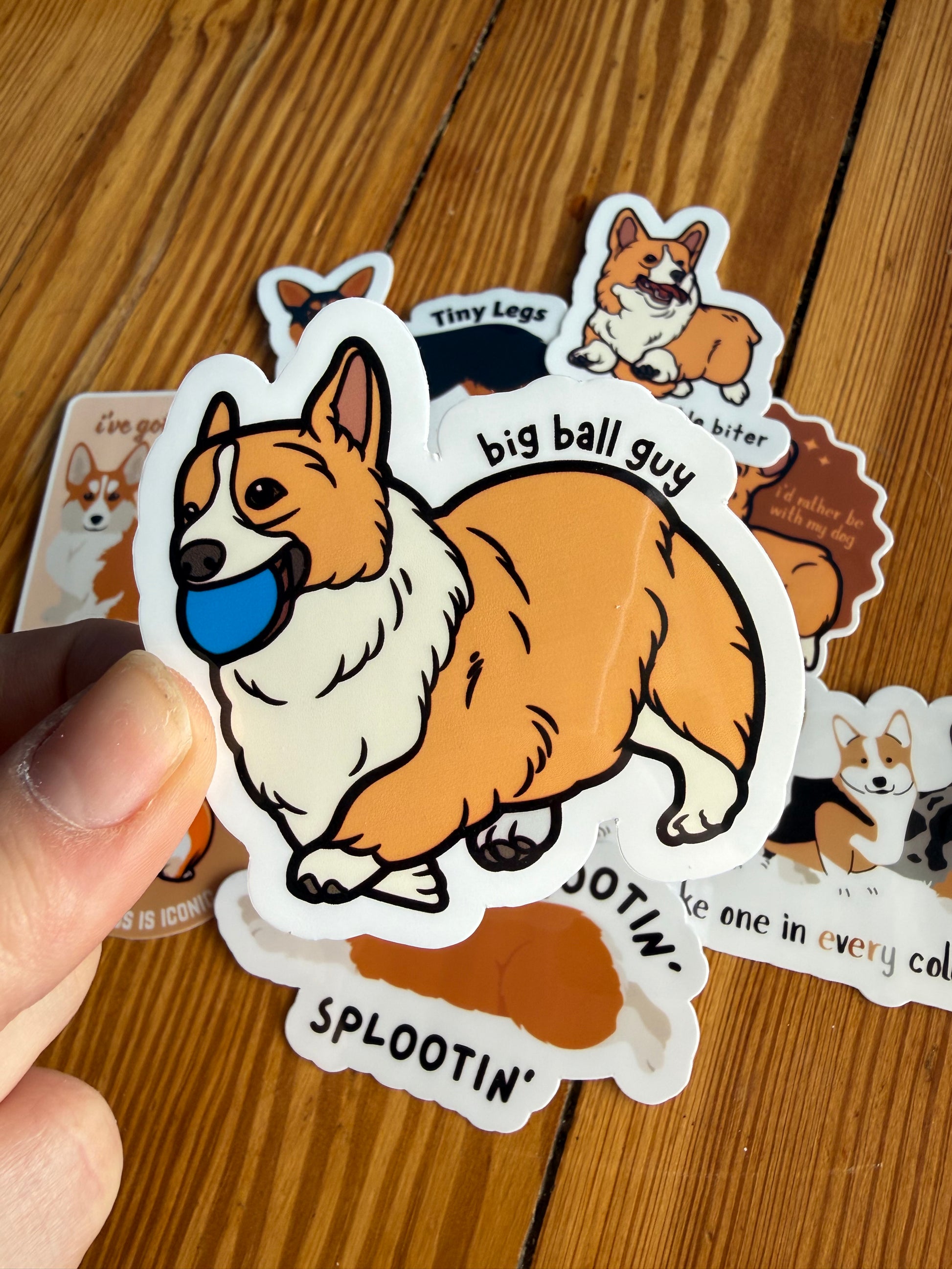 "Big Ball Guy": Close-up of a sticker depicting a corgi happily holding a bright blue ball in its mouth with the text "Big ball guy."
