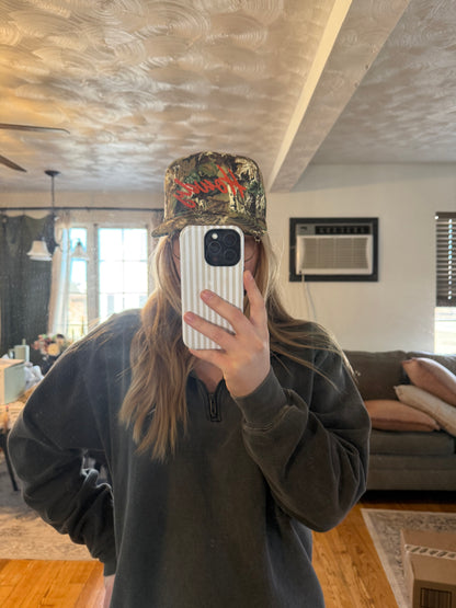 A lifestyle mirror selfie of a girl in a living room wearing a camo "Howdy" hat and a gray quarter-zip sweatshirt. This casual everyday outfit photo shows how the hat fits and styles with loungewear for a trendy, oversized look.