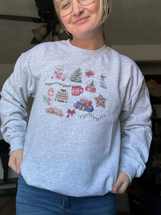 girl wearing ash gildan 18000 christmas cat collage crewneck sweatshirt, festive watercolor cats and holiday illustrations, cozy winter cat mom gift sweater styled with jeans, unique artistic cat christmas sweatshirt for women, trendy holiday outfit idea for cat lovers