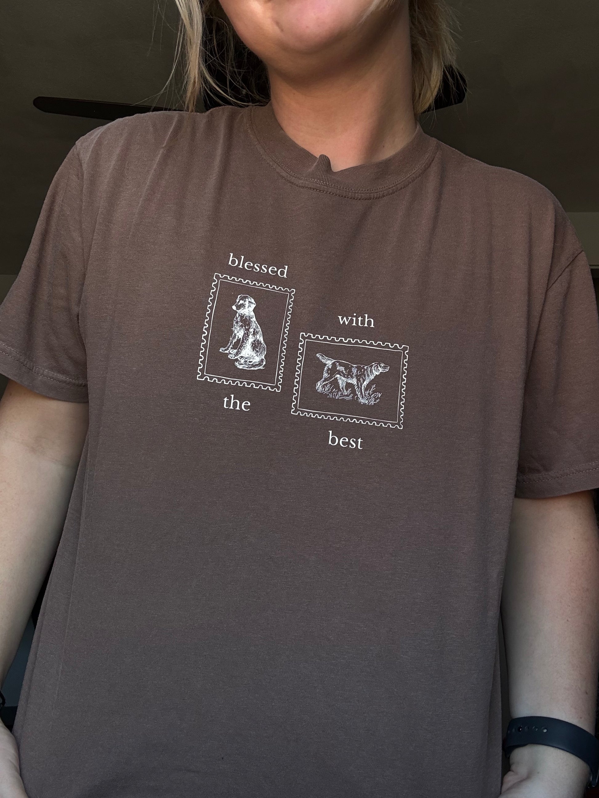 Person wearing a brown shirt with Blessed with the Best text and graphic of two stamps with dogs on them.