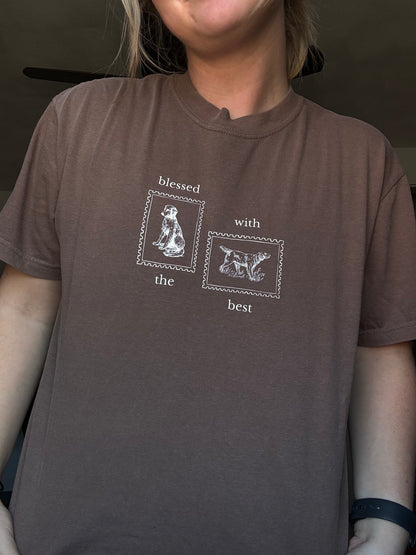 Person wearing a brown shirt with Blessed with the Best text and graphic of two stamps with dogs on them.
