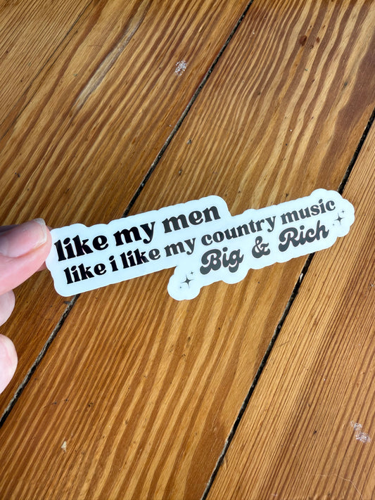 Hand holding a funny country music quote sticker that reads “I like my men like I like my country music, Big & Rich,” displayed against a rustic wooden background. This waterproof vinyl sticker features bold typography and a playful southern humor design, perfect for country music lovers, western aesthetic fans, Nashville style gifts, laptop stickers, water bottle decals, and sarcastic country girl accessories.