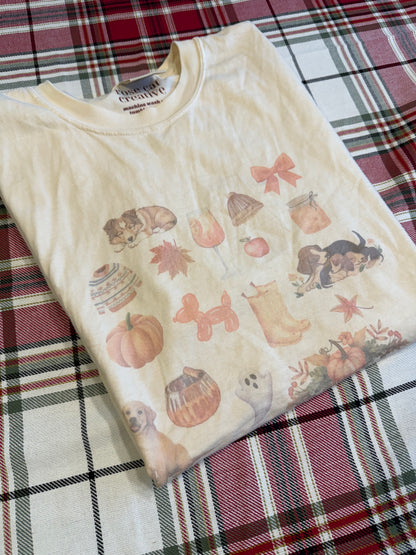 Flat lay of Comfort Colors ivory fall dog collage t-shirt on red plaid blanket. Sublimated watercolor fall and dog themed graphic tee for pet lovers. Cozy autumn apparel photography with rustic farmhouse fall accents. Perfect fall dog mom aesthetic shirt for gift giving, Thanksgiving outfits, and seasonal wardrobe updates.