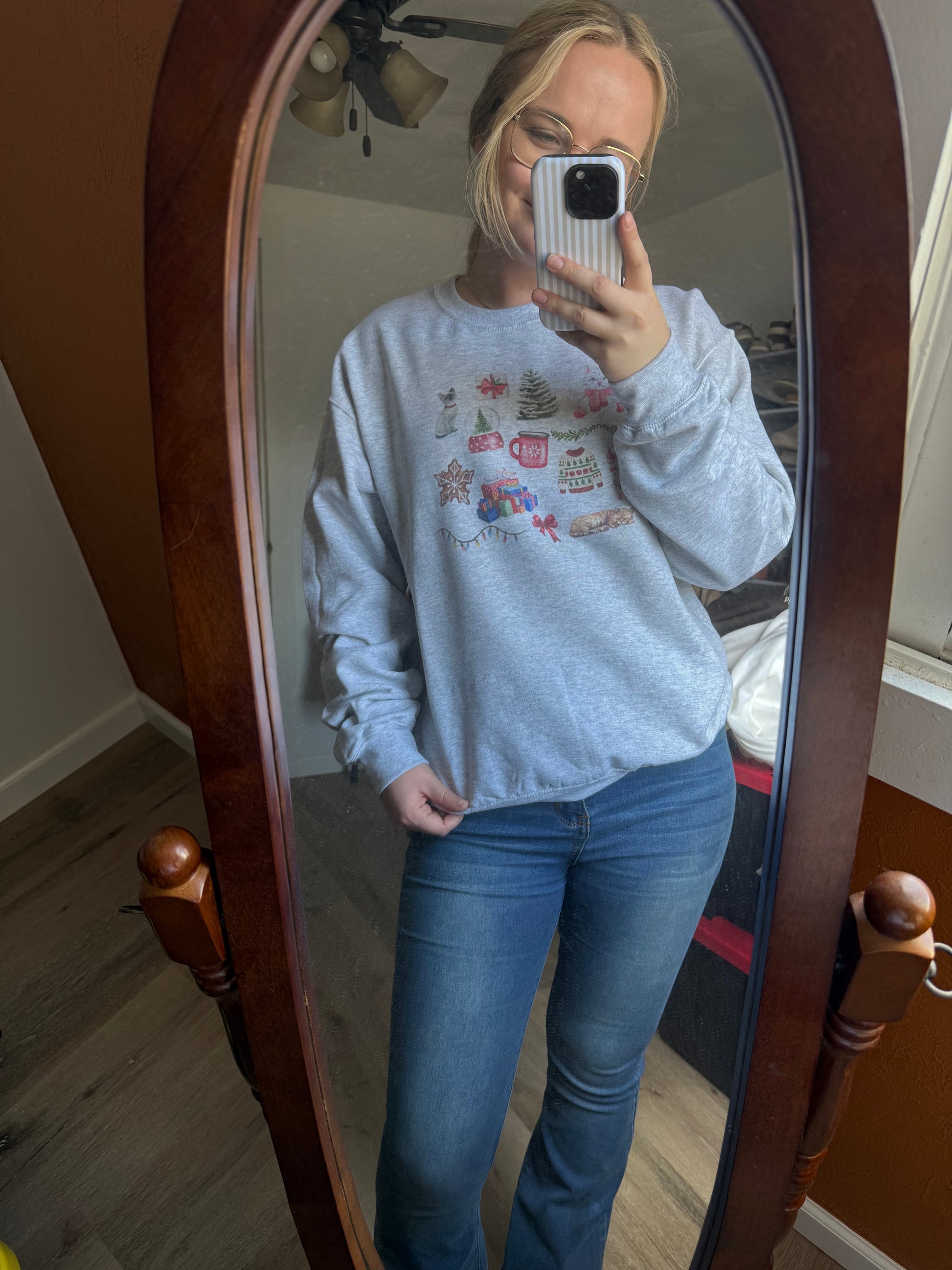 christmas cat watercolor collage sweatshirt worn by girl in jeans taking a mirror selfie, ash gray gildan crewneck featuring artistic holiday cat illustrations, perfect cozy winter outfit for cat moms, long tail christmas cat sweatshirt gift idea for women who love cats