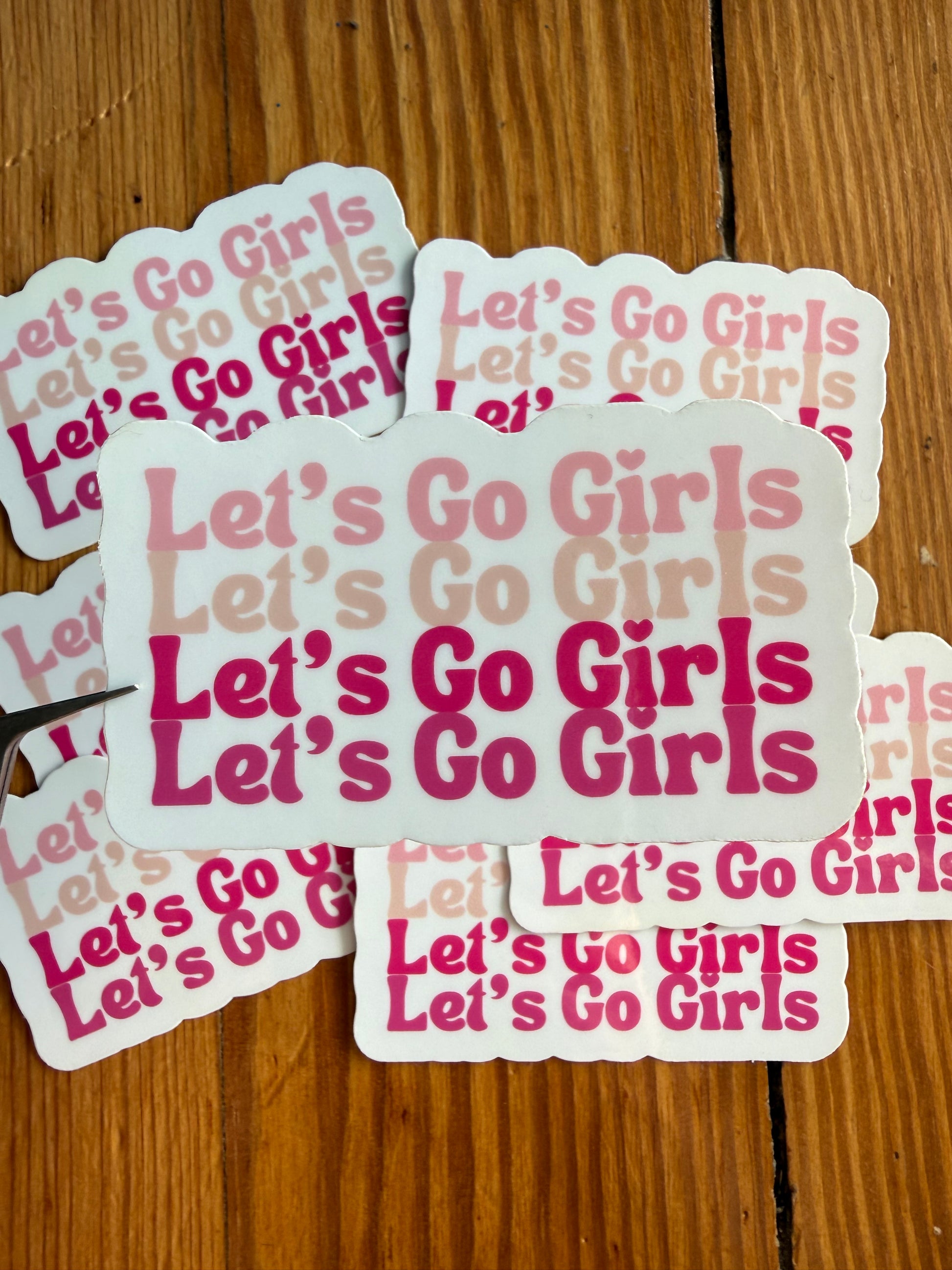 Let’s Go Girls pink western vinyl sticker in front of multiple stickers, cowgirl aesthetic sticker with bold pink typography, trendy country girl accessory sticker for water bottles, notebooks, laptops and gifts