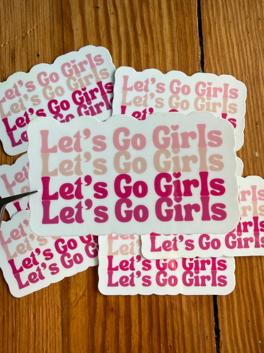 Let’s Go Girls pink western vinyl sticker in front of multiple stickers, cowgirl aesthetic sticker with bold pink typography, trendy country girl accessory sticker for water bottles, notebooks, laptops and gifts