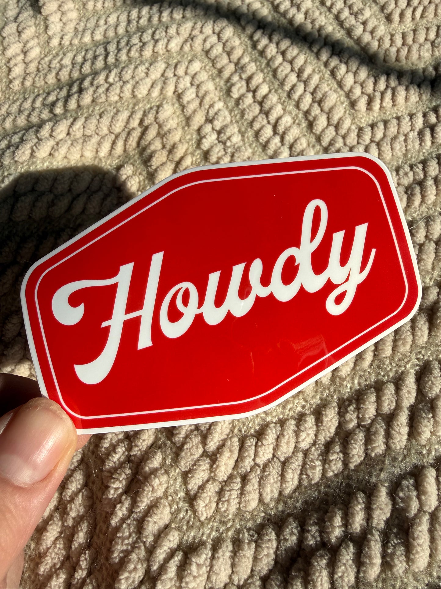 Handheld "Howdy" sticker with bold red background; minimalist western typography decal, waterproof and scratch-resistant for phone cases.