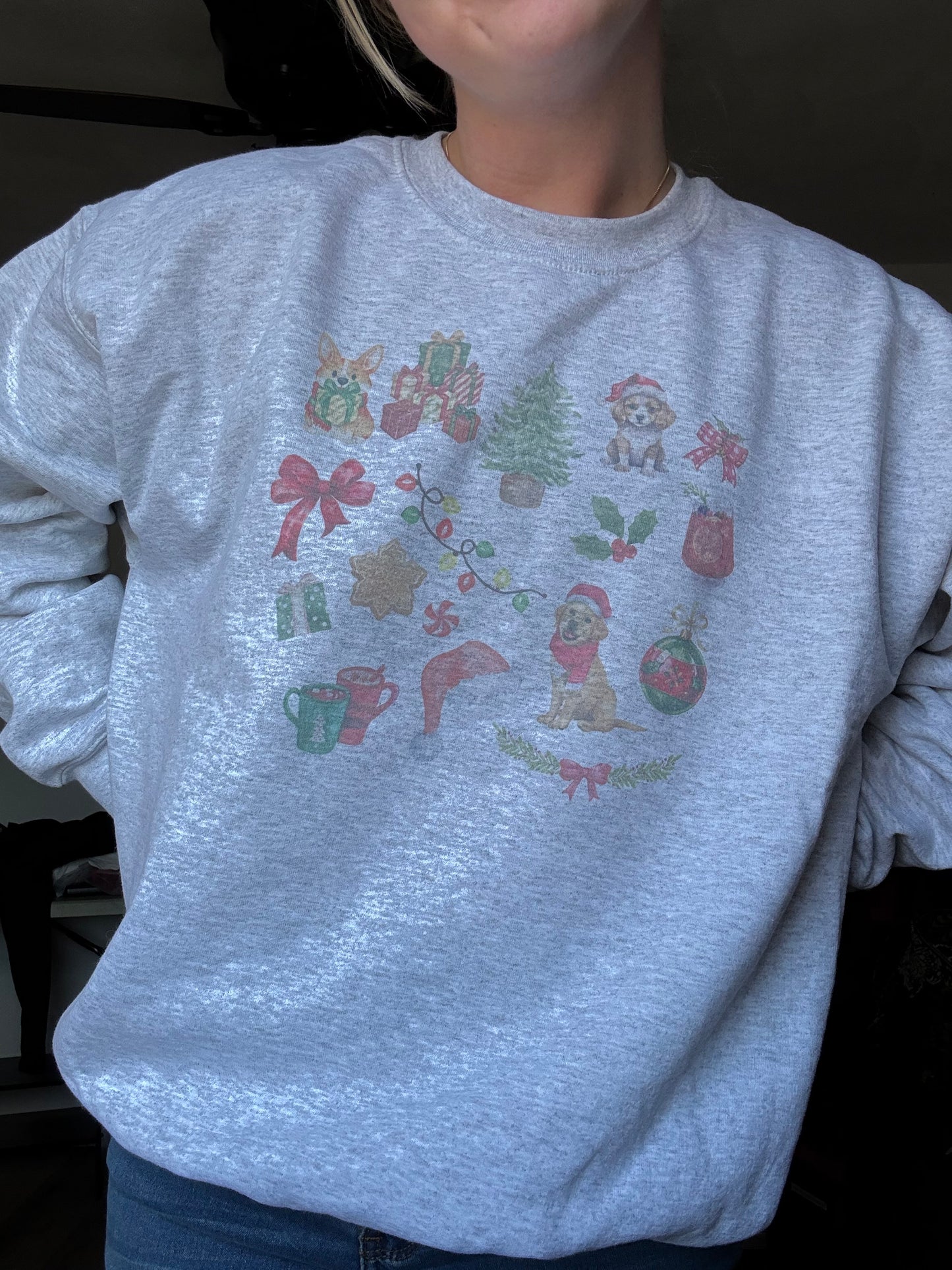 Person wearing Ash Gildan 18000 crewneck featuring watercolor dog and Christmas art, cozy winter dog mom sweatshirt for holiday season, unisex Christmas dog lover gift, festive watercolor dog collage sweater worn for casual holiday fashion.