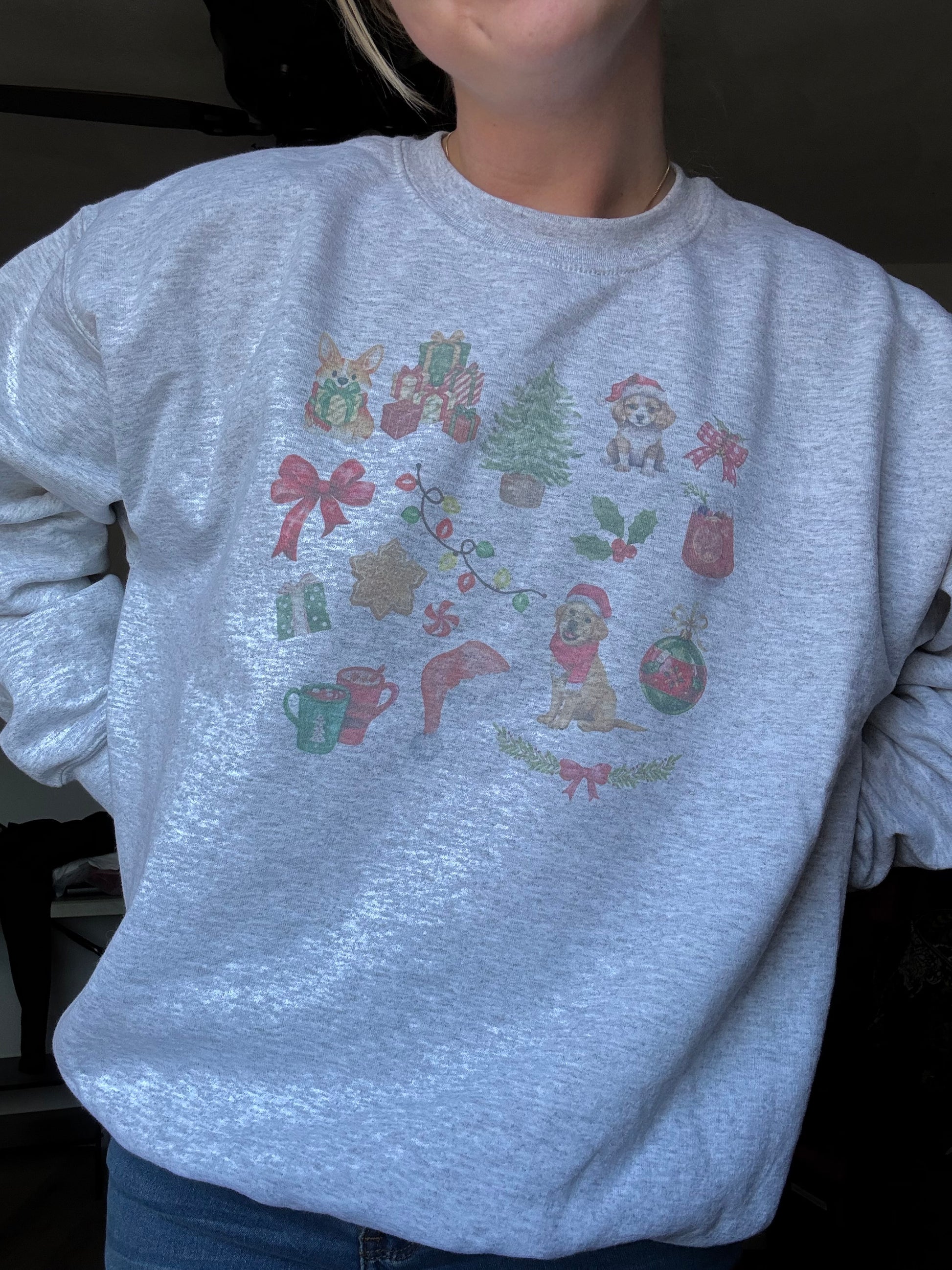 Person wearing Ash Gildan 18000 crewneck featuring watercolor dog and Christmas art, cozy winter dog mom sweatshirt for holiday season, unisex Christmas dog lover gift, festive watercolor dog collage sweater worn for casual holiday fashion.