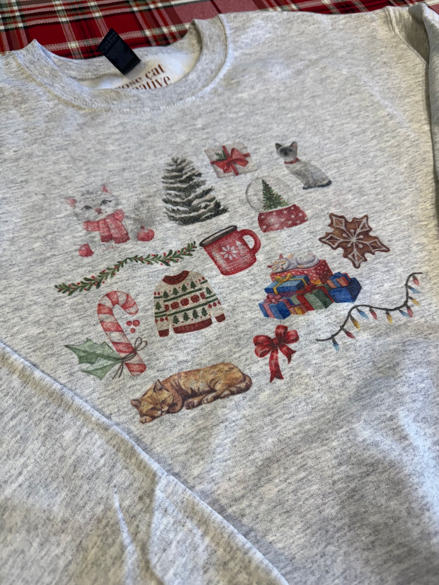 laid flat ash christmas cat watercolor collage sweatshirt on red plaid backdrop, gildan 18000 crewneck with festive cat artwork, unique artistic cat lover holiday gift, cozy winter sweatshirt with watercolor christmas illustrations for cat enthusiasts