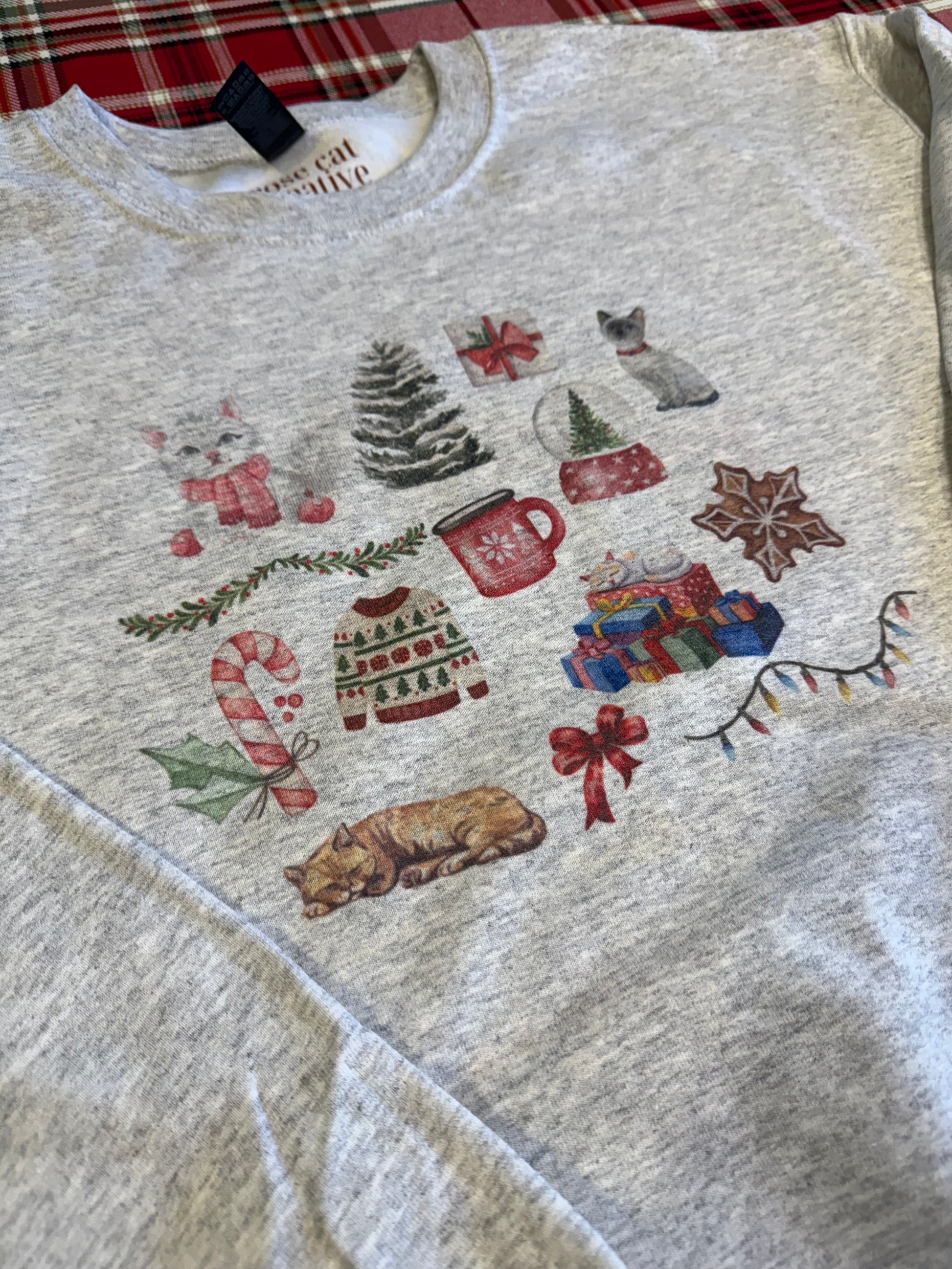 laid flat ash christmas cat watercolor collage sweatshirt on red plaid backdrop, gildan 18000 crewneck with festive cat artwork, unique artistic cat lover holiday gift, cozy winter sweatshirt with watercolor christmas illustrations for cat enthusiasts