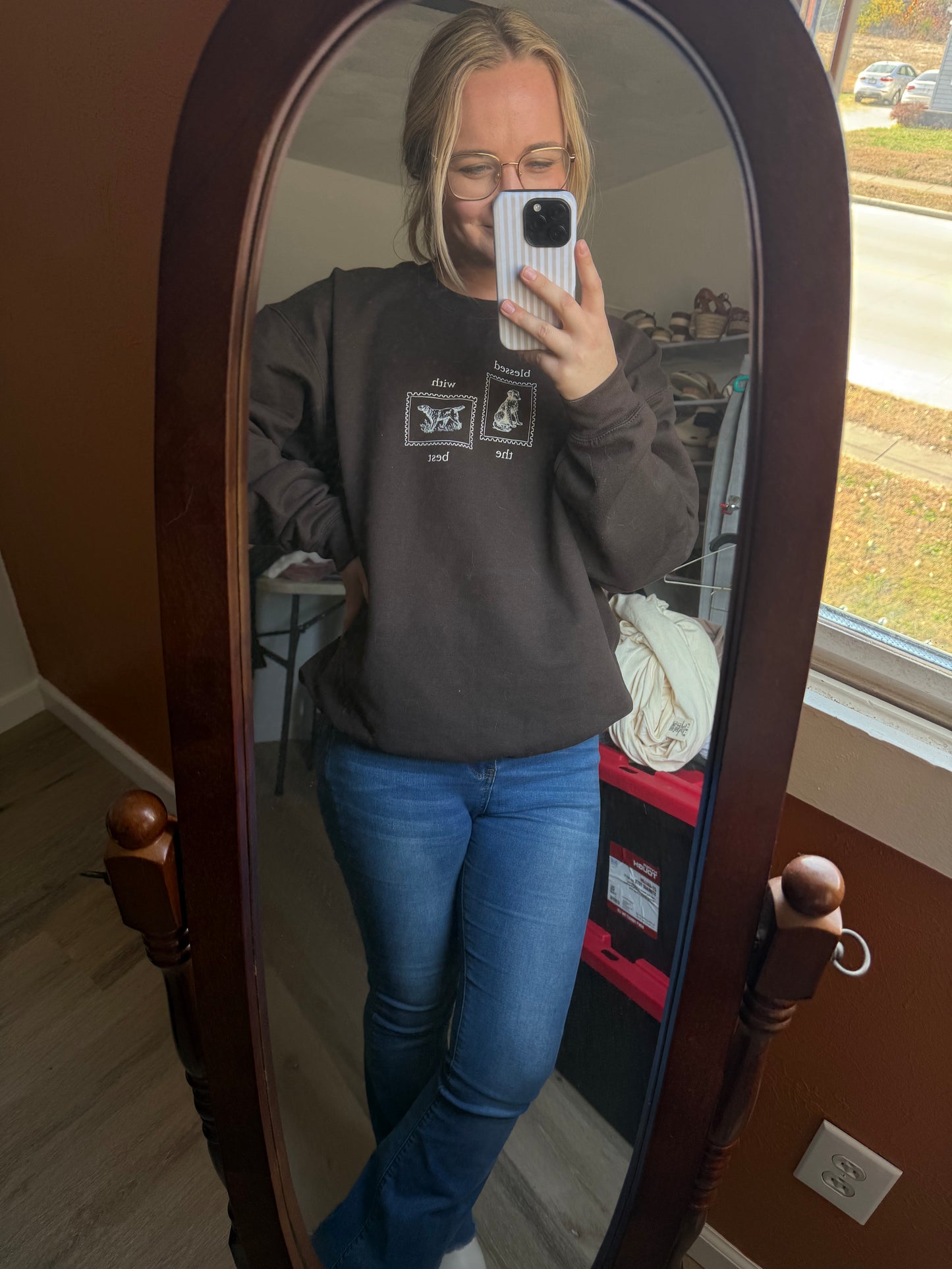 Person taking a mirror selfie wearing a dark brown sweatshirt and blue jeans. The sweatshirt has a tan DTF design that says Blessed with the Best and has dog stamp designs. The sweatshirt is perfect for dog parents that love talking about their furry friends.