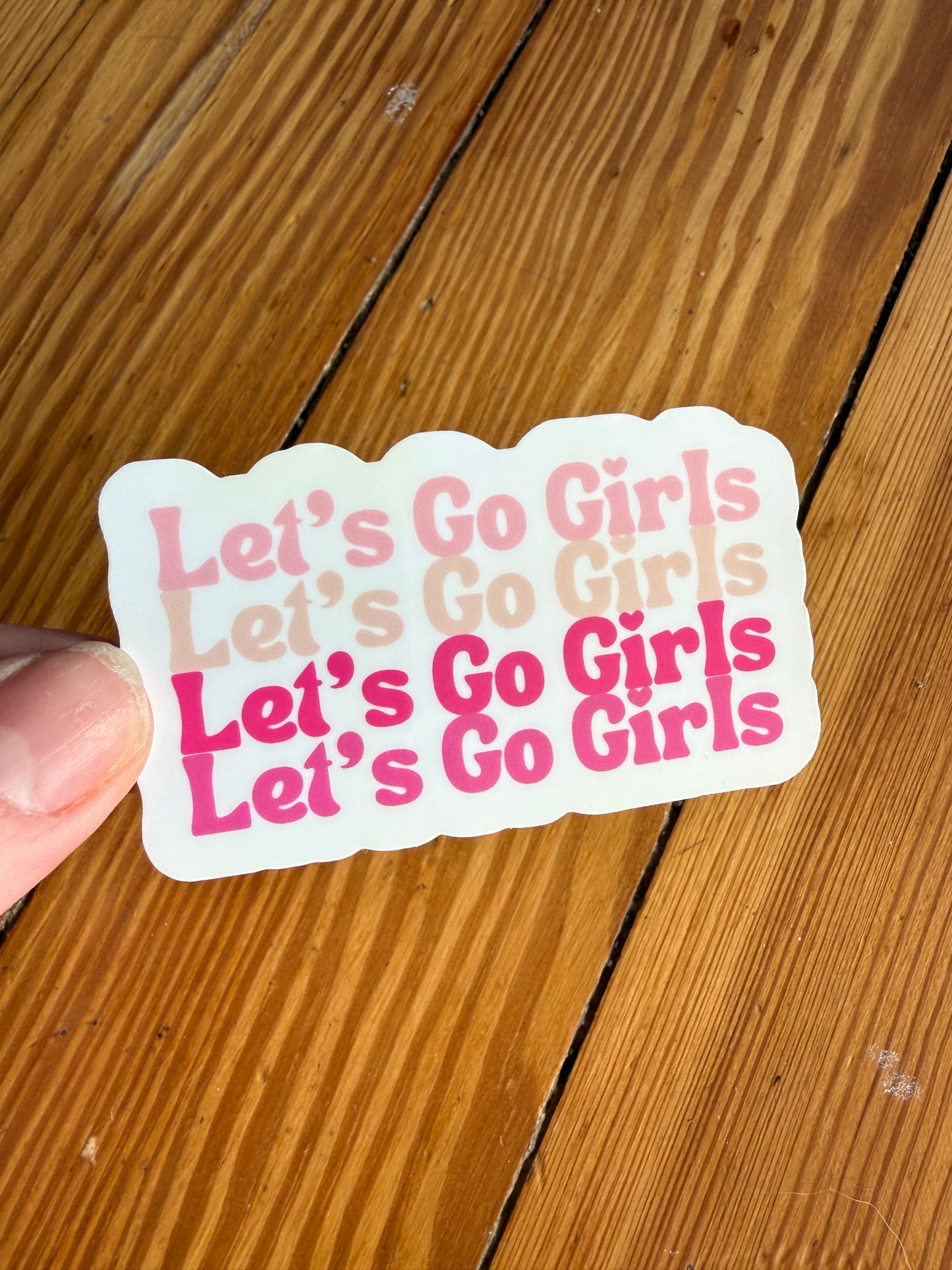 Let’s Go Girls pink typography sticker on wooden background, western cowgirl aesthetic vinyl sticker with four Let’s Go Girls phrases in different shades of pink, country girl sticker for water bottle, laptop, journal, pink cowgirl decor sticker