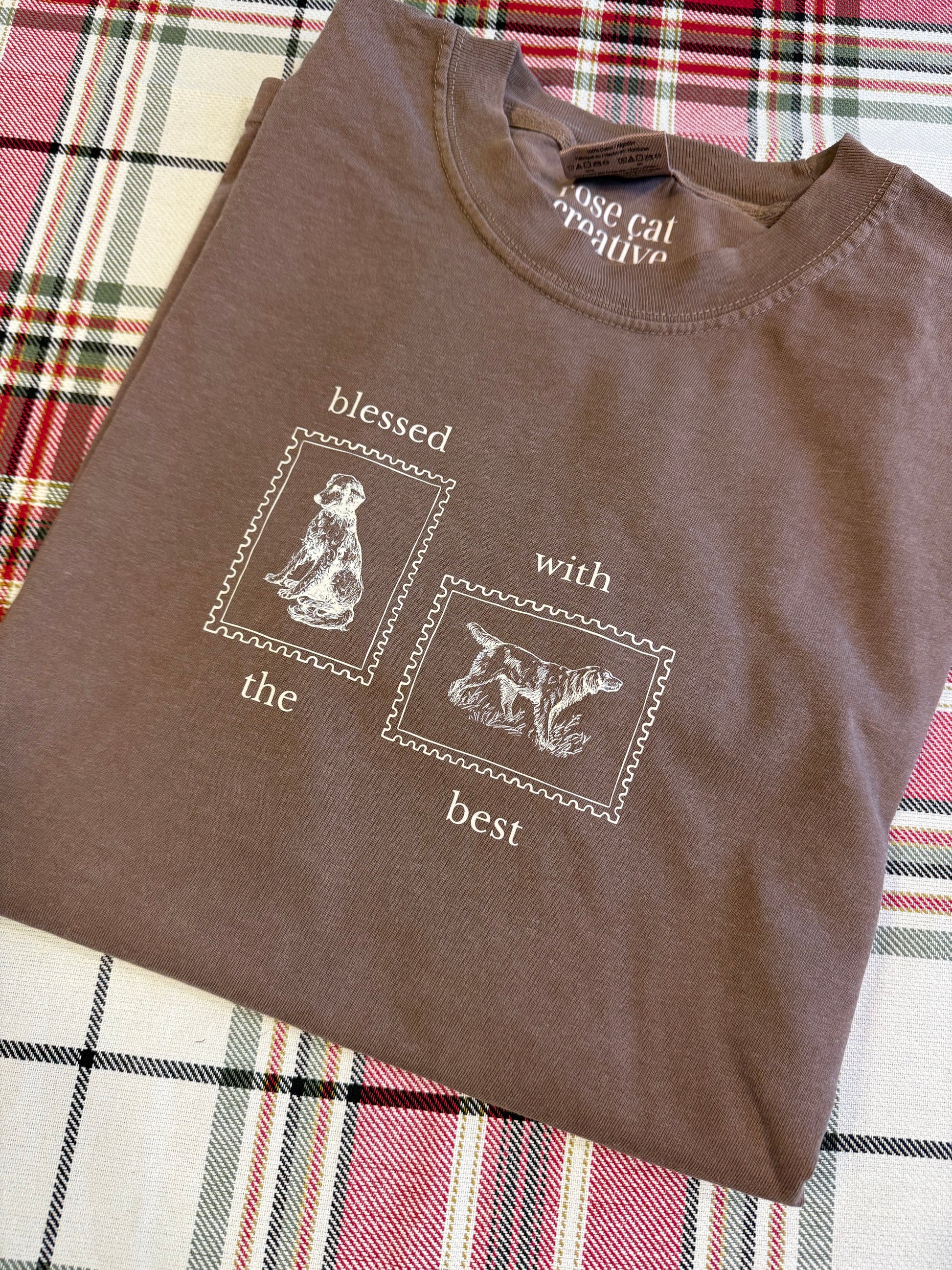 Brown t-shirt with tan dog-themed design on a plaid fabric background
