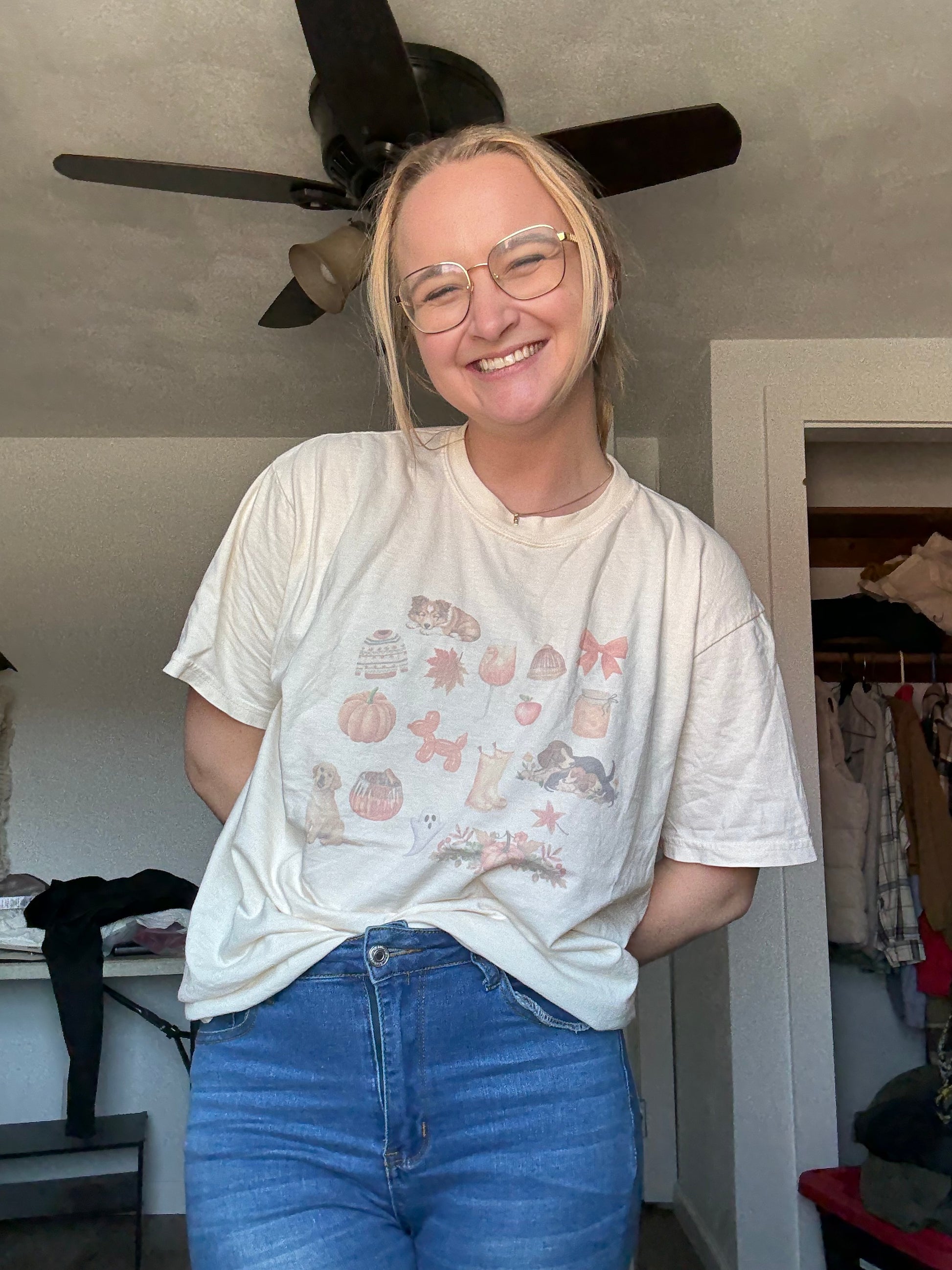 Girl wearing Comfort Colors ivory shirt with watercolor dog and fall illustration collage, styled with denim jeans. Rustic dog mom fall aesthetic tee for pumpkin patch, hayrides, Thanksgiving, and cozy autumn days. Long tail keyword fall dog graphic tee for women who love pets and neutral aesthetic apparel.